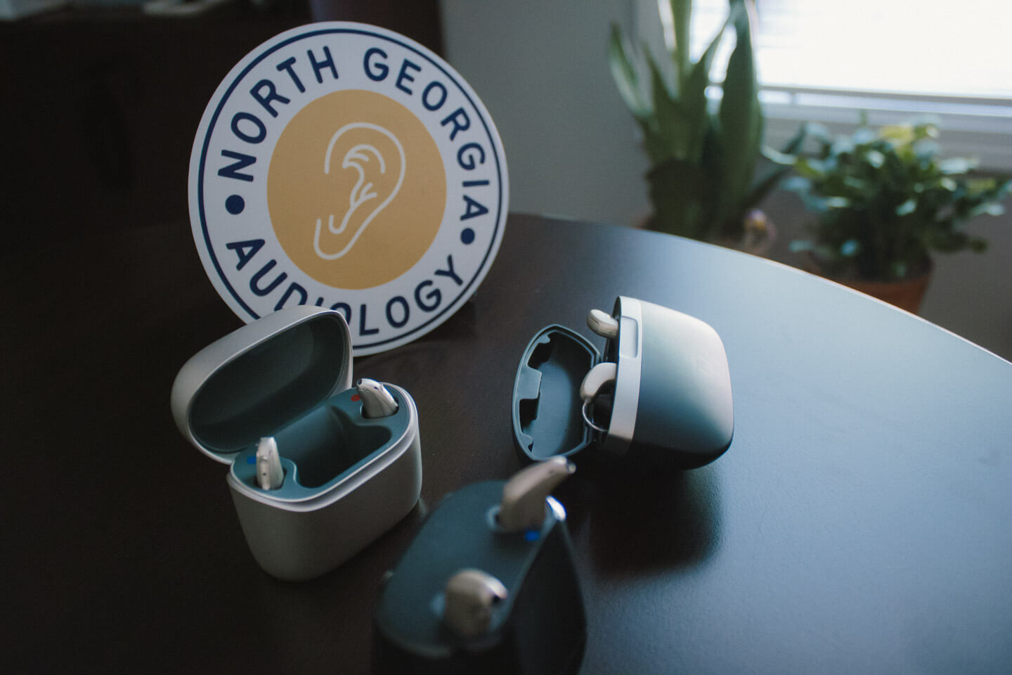 3 types of hearing aids on a table in their cases with a sign that says North Georgia Audiology in the background
