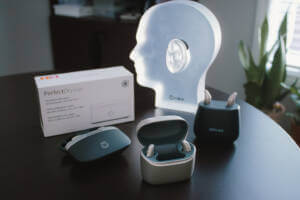 3 Types of hearing aids on a table with a model of a head wearing a hearing aid to show it it'll look wearing it